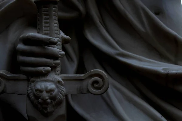 sculpture.  female hand holds a sword.  dark background