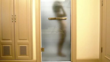 Genç kadın kız duş şeffaf cam banyo kapı arkasında sonra saç kurutma bir otel odasında bulanık silüeti. statik yan vurdu