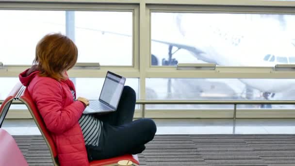 若いきれいな女性フリーランス オフィスの外のプロジェクトの難しい空港ターミナルとノート パソコンを動作に座って出発を待っています 背景に外飛行機を燃え尽きる側のハンドヘルド ショット — ストック動画