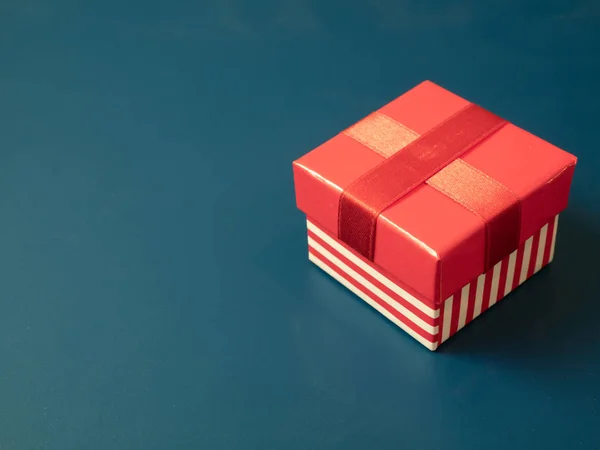 简单的小礼品盒与红色条纹和丝带在蓝色背景 — 图库照片