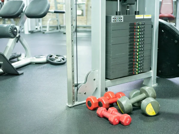 few light weight dumbbells on a gym floor near heavy weight cross training machine. woman personal training lose weight or get in shape concept