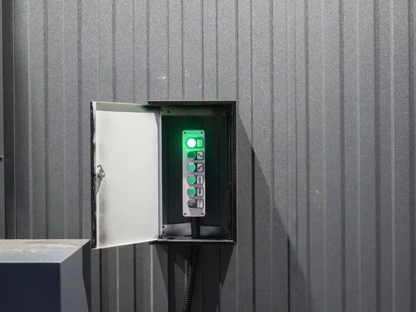 opened box with industrial lift elevator control board at warehouse or factory, lot of buttons with gray wall on background. green light is on as a indicator of work in progress