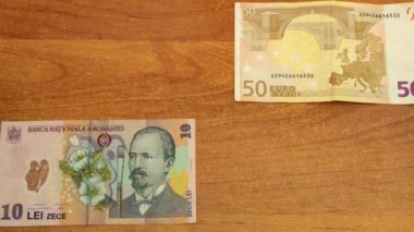 Motion animasyon 50 € ve 10 Romence lei ahşap masanın üstüne bırak. farklı yönden hareket banknotlar için bir saniye ve daha sonra önünden hareketli ortasında buluş. closeup 4 k video ilmekledi