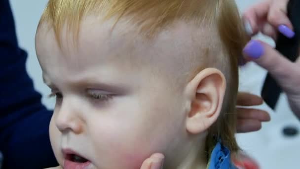 Hairdresser with trimmer cutting hair of 2 years old boy while child's mom blow away cutted hair. close-up macro 4k handheld footage — Stock Footage Hairdresser Trimmer Cutting Hair Years Old Boy While Child Mom Stock Footage
