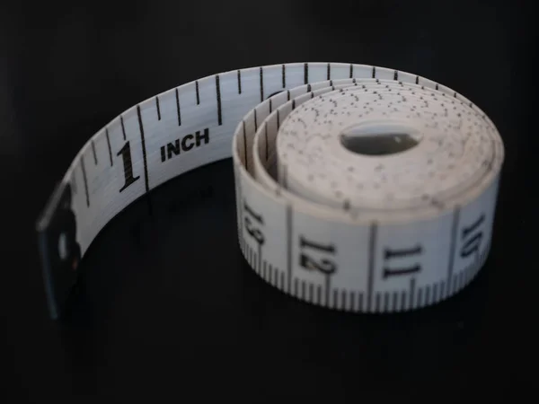 クローズ アップ テーラーが黒い背景に分離したテープを測定します。最初の 1 インチ表示と残りの部分、丸くなって丸いコイルのボビンのスパイラルに巻いて — ストック写真