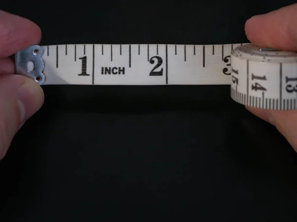 Macro extremo close-up de dedos do homem segurando régua fita métrica com poucos centímetros desenrolados no fundo preto escuro — Fotografia de Stock