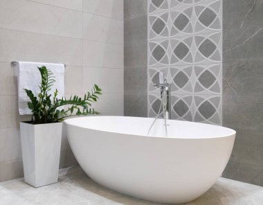 Beyaz taş küvet, gri fayans duvar, yeşil bitki ve havlu ile askı ile seramik saksı ile modern banyo iç tasarım