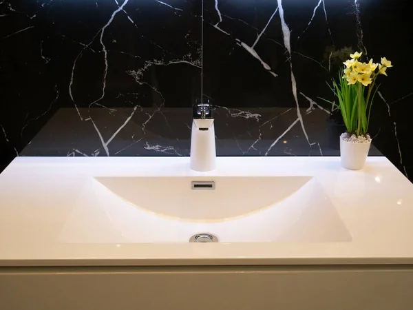 Κοντινό πλάνο του σύγχρονου μπάνιου καθαρό λευκό νιπτήρα με βρύση χρωμίου και βάζο με λουλούδια. τοίχος από μαύρο μάρμαρο — Φωτογραφία Αρχείου