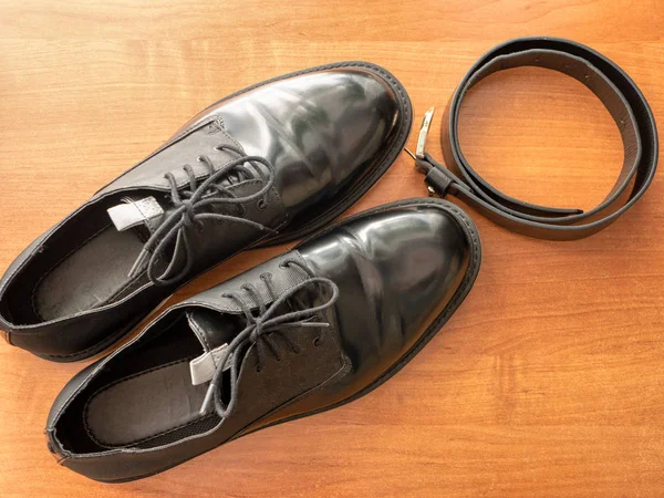 木製のテーブルの上にエレガントな光沢のある黒のフォーマルな男性の靴と革のベルトのペア — ストック写真