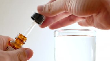 ellerin pipet ile küçük şişe ilaç küçük miktarda alarak yakın çekim ve berrak su ile şeffaf cam içine birkaç damlacık düştü. 4k video görüntüleri