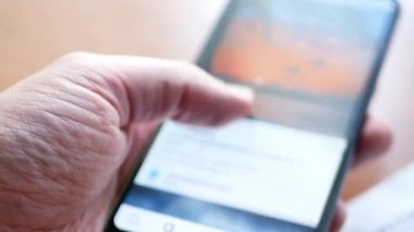 açılan uygulama ünlü sosyal ağ kaydırma ve fotoğrafları çift dokunarak, mesajları sevme ile akıllı telefon tutan adam. makro yakın çekim 4k video. adamın eline seçici odak, cep telefonu bulanık