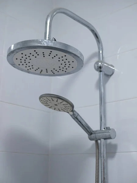 Beyaz fayans banyodaki iki duş başlığının yakın plan görüntüsü. Metal boruya büyük ve esnek hortuma küçük bağlıdır.