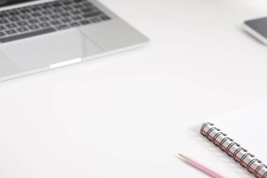 sarmal defter, pembe renkli kalem ve klavye dizüstü bilgisayarı beyaz bir masa yüzeyinde.