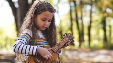 Portrait of little girl playing ukulele in the street autumn fall happy moments guitar close up child kid clipart