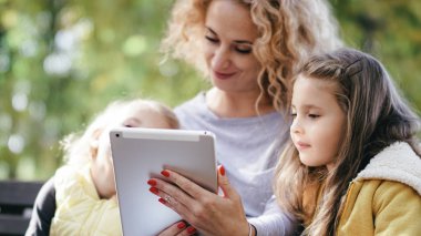 Anne ve kızları tablete bakıyor ve gülümsüyor çizgi film reklamları çocuklar aile teknolojisi mutlu anlar çocuklar