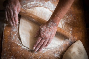 Kızın elleri ahşap bir masanın üzerinde un bulunan bir oklavayı tutuyor. Çiğ hamuru dışarı atıyor. Pizza turtası ezmesi için uygun.