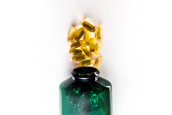黄色药丸胶囊从绿色塑料瓶中溢出 维生素E Omega 关于白人背景 图库图片
