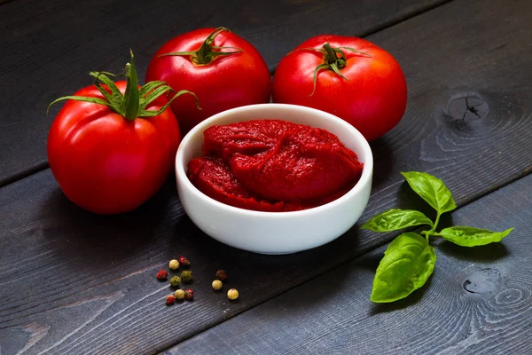 Tomatoes and tomato paste on a dark background, basil and spices.