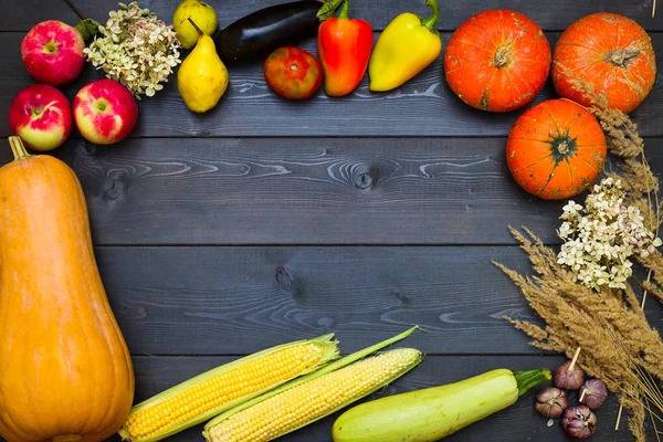 Thanksgiving Day. Frame made of vegetables and fruits. Gifts of autumn. Place for inscription. Dark wooden background, noble colors. Pumpkin, corn, garlic, apples, eggplants, flowers, lemon, tomatoes, peppers, pears. Autumn vegetables and fruits. Foo