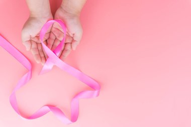 Kadın elleri pembe arka planda pembe göğüs kanseri tutuyor.