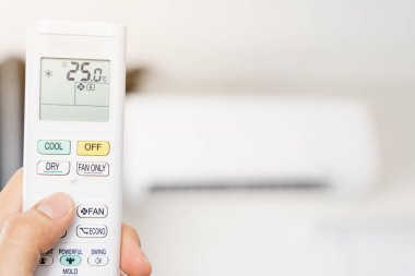 İnsan eli odadaki klimayı açmak ya da ayarlamak için beyaz klima kumandası kullanıyor..