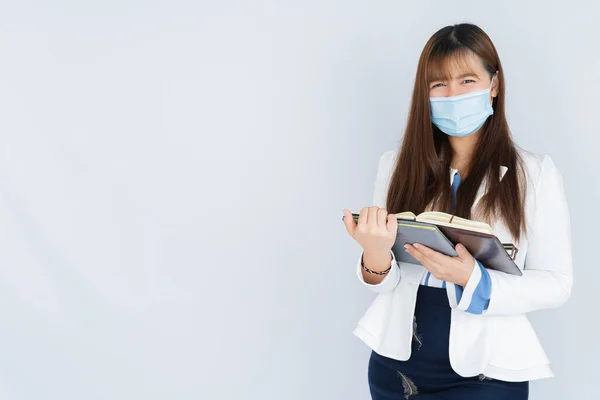 微笑的亚洲女商人戴着医疗面罩 手里拿着笔记本 在灰色背景下看着相机 回到正常的概念 — 图库照片
