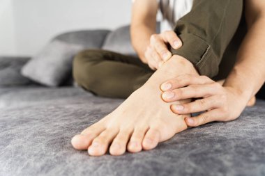 Genç adam evdeki kanepede otururken ayak bileği ağrısından muzdarip. Sağlık hizmeti tıbbi veya günlük yaşam konsepti.