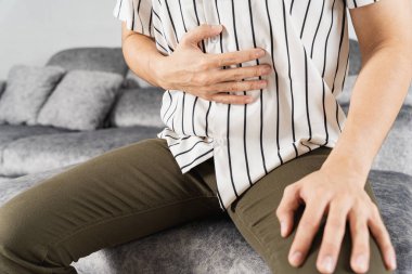 Evdeki kanepede otururken karın ağrısı çeken genç bir adam. Sağlık hizmeti tıbbi veya günlük yaşam konsepti.