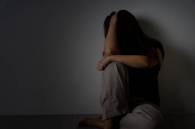 Üzgün kadın, karanlık bir odada tek başına otururken dizine sarılıp ağlar. Depresyon, mutsuz, stresli ve anksiyete bozukluğu.