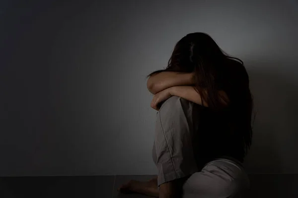 Üzgün kadın, karanlık bir odada tek başına otururken dizine sarılıp ağlar. Depresyon, mutsuz, stresli ve anksiyete bozukluğu.