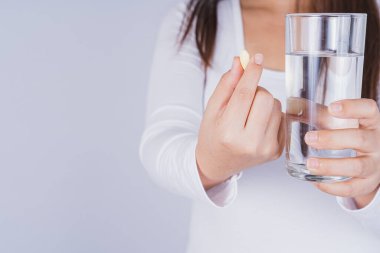 Gri arka planda elinde bir bardak su ve hap tutan Asyalı kadın. Sağlık ve tıbbi eczane kavramı