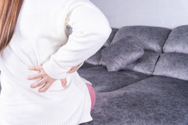 Evdeki kanepede otururken sırt ağrısı çeken genç bir kadın. Sağlık hizmeti tıbbi veya günlük yaşam konsepti.