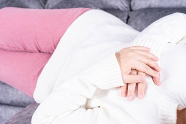 Evdeki kanepede otururken kalp ağrısı çeken genç bir kadın. Sağlık hizmeti tıbbi veya günlük yaşam konsepti.