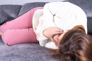 Evdeki kanepede otururken kalp ağrısı çeken genç bir kadın. Sağlık hizmeti tıbbi veya günlük yaşam konsepti.