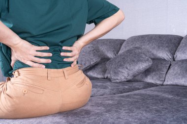 Evdeki kanepede otururken sırt ağrısı çeken genç bir adam. Sağlık hizmeti tıbbi veya günlük yaşam konsepti.