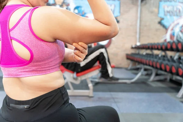 Woman holding hand excessive fat arm at gym. Woman pinching arm fat flabby skin. Weight loss, slim body, healthy lifestyle concept.