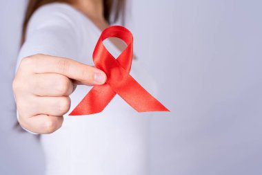 Kızıl AIDS farkındalık kurdelesi gri arka plandaki adamın elinde. Dünya Yardım Günü, Sağlık ve Tıbbi Konsept.