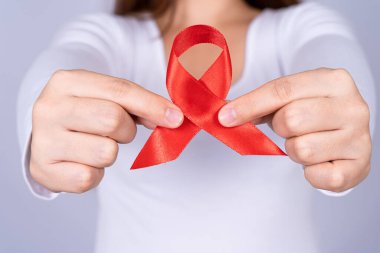 Kızıl AIDS farkındalık kurdelesi gri arka plandaki adamın elinde. Dünya Yardım Günü, Sağlık ve Tıbbi Konsept.