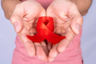 Kızıl AIDS farkındalık kurdelesi gri arka plandaki adamın elinde. Dünya Yardım Günü, Sağlık ve Tıbbi Konsept.