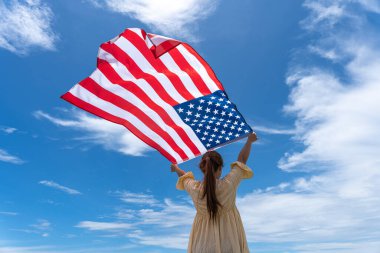 Mavi gökyüzünün altında bayrak tutan ve ayakta duran kadın.