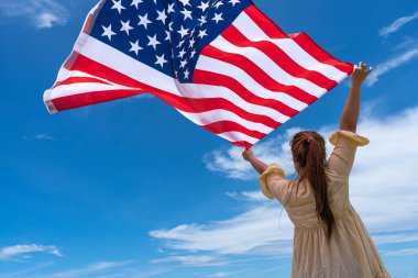 Mavi gökyüzünün altında bayrak tutan ve ayakta duran kadın.