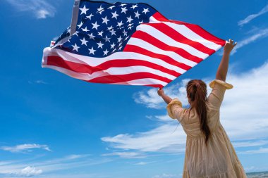 Mavi gökyüzünün altında bayrak tutan ve ayakta duran kadın.