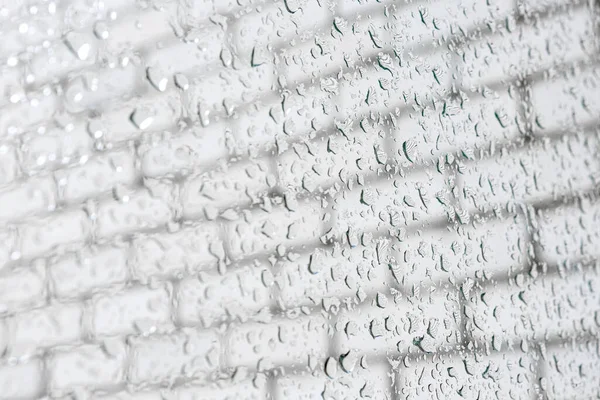 Raindrops on a window pane. Drops flow down. Cloudy weather, it is raining. Bright textured background. Macro shot of raindrops. Wet glass surface. Fluid flows through the window. Raindrops texture.