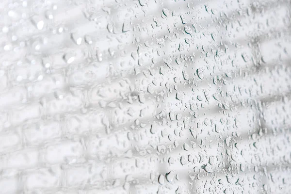 Raindrops on a window pane. Drops flow down. Cloudy weather, it is raining. Bright textured background. Macro shot of raindrops. Wet glass surface. Fluid flows through the window. Raindrops texture.