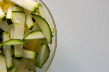 Beyaz arka planda şeffaf bir tabakta dilimlenmiş kabak dilimleri. Çiğ vejetaryen yemeği. Kabağı küçük dilimlere ayır. Ham ürün, yeşil kabuk..