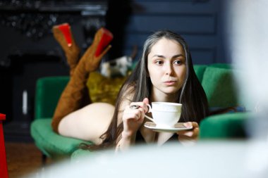 Avrupa görünümlü güzel, çıplak bir esmer elinde bir fincan çayla yeşil bir kanepede yatıyor. Bir fincan çay ve bir fincan çayın ellerinde. Ayakta uzun kahverengi çizmeler. Güzellik ve cinsellik.