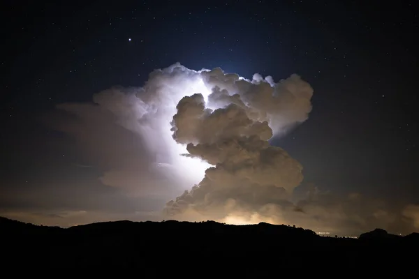 Lightning strikes inside a cloud cluster at night seen from far away