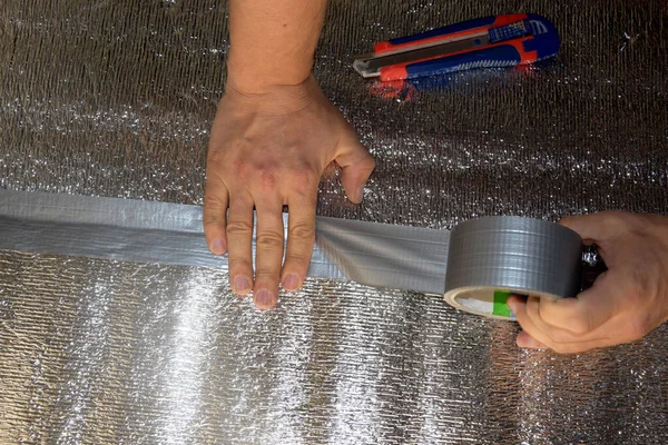 一个男人用胶带把一个铝箔等索藏起来 男性手握着强化带子 修理公寓 地板保温材料 免版税图库照片