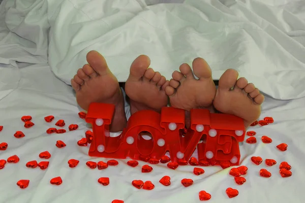 白いシートの上に裸の足 男と女の足 愛のカップルの素足の背景にある言葉の愛と多くの小さな 赤い心 — ストック写真