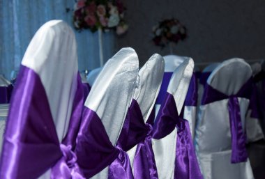 Sandalyeler beyaz bez ve büyük mor saten fiyonklarla süslenmiş. Restoran partisinde sandalyenin arkasına ipek fiyonk bağlanmıştı. Beyaz kumaş kaplamalı sandalyeler..